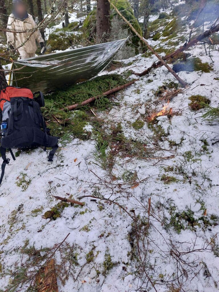 Avaruuslakana katoksena ja havupeti hätämajoitteena lumisessa metsässä.